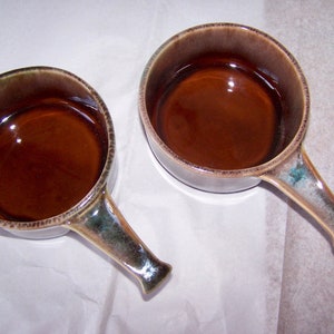 May include: Two brown ceramic soup bowls with handles. The bowls have a mottled brown glaze with green and blue accents.