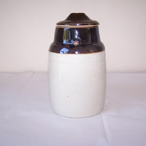 May include: A white ceramic crock with a brown glazed lid. The crock has a speckled white finish and a brown band around the top.