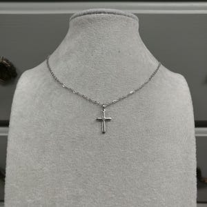 Pode incluir: Um colar de corrente de prata com um pequeno pingente de cruz de prata.
