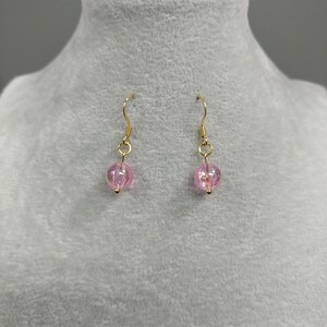 May include: A pair of gold dangle earrings with pink glass beads. The beads are round and have a slight shimmer.