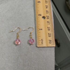 May include: A pair of gold dangle earrings with pink iridescent glass beads.