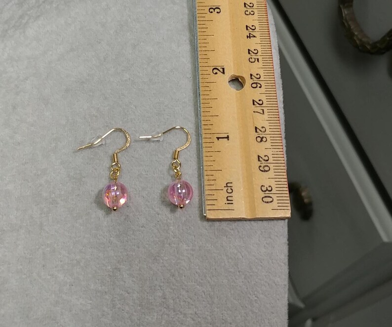 May include: A pair of gold dangle earrings with pink iridescent glass beads.