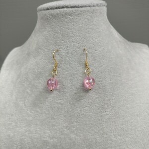 May include: A pair of gold dangle earrings with pink glass beads.