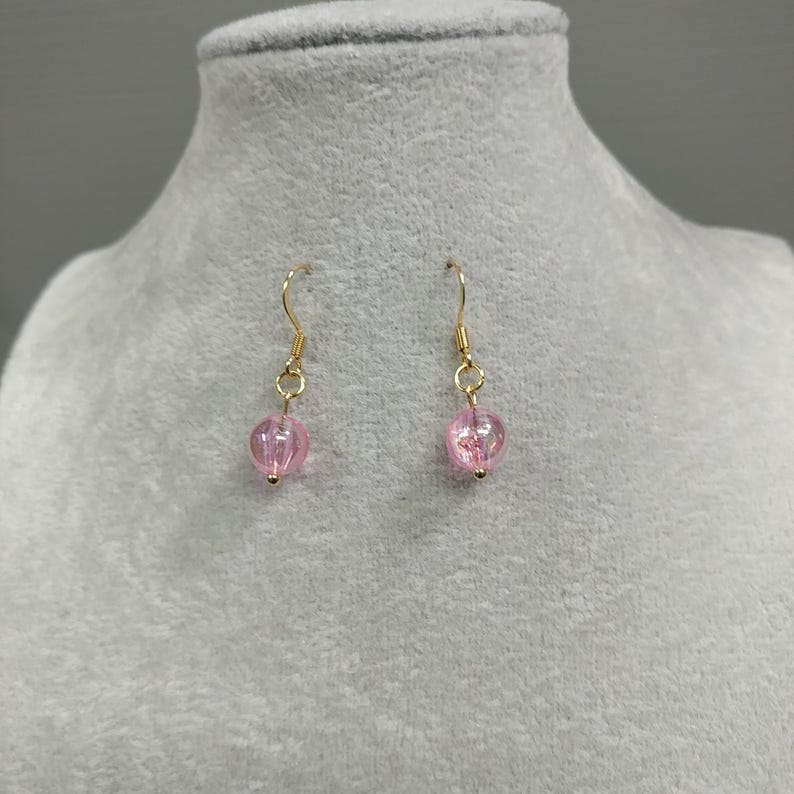 May include: A pair of gold dangle earrings with pink glass beads.