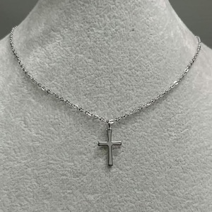 Pode incluir: Um colar de corrente de prata com um pequeno pingente de cruz de prata.