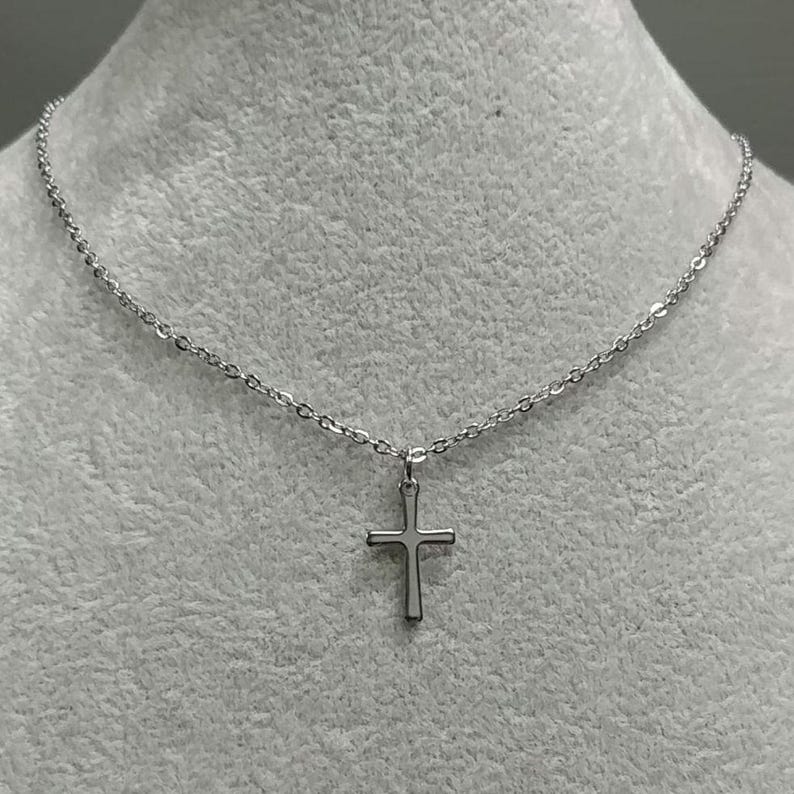 Pode incluir: Um colar de corrente de prata com um pequeno pingente de cruz de prata.