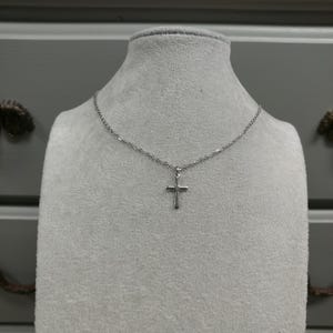 Pode incluir: Um colar de corrente de prata com um pequeno pingente de cruz de prata.