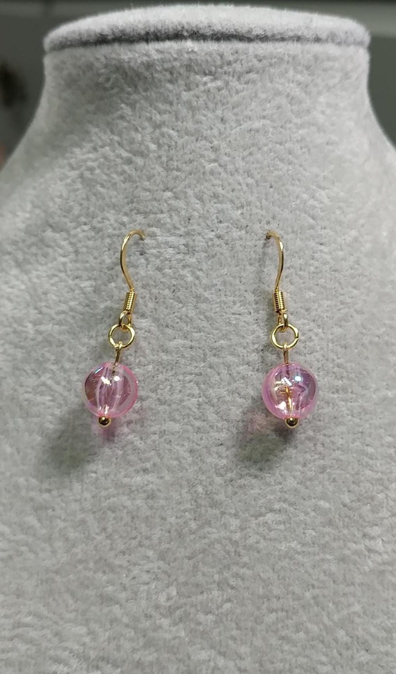 May include: A pair of gold dangle earrings with pink glass beads. The beads have a shimmery finish.