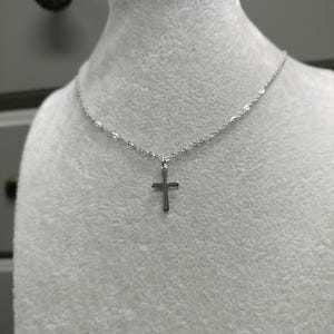 Pode incluir: Um colar de corrente de prata com um pequeno pingente de cruz de prata.
