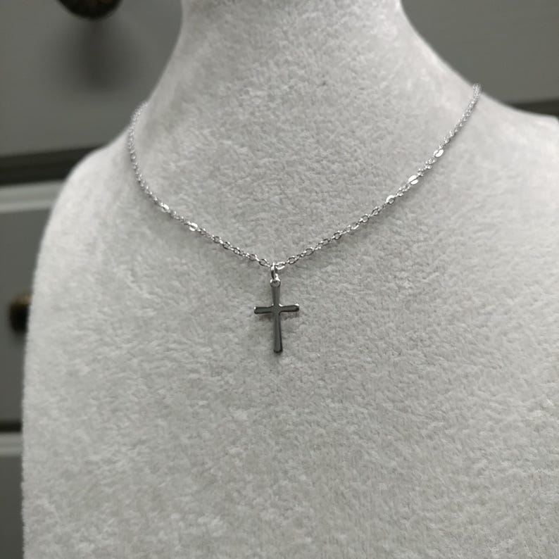 Pode incluir: Um colar de corrente de prata com um pequeno pingente de cruz de prata.