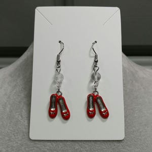 May include: A pair of silver dangle earrings with red shoe charms and clear crystal beads.