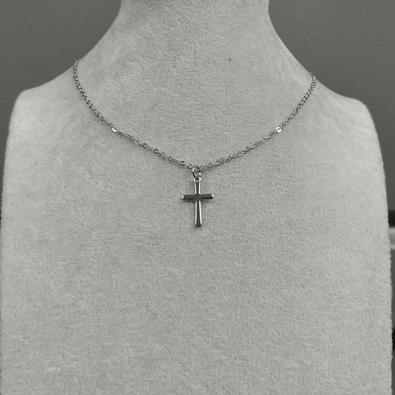 Pode incluir: Um colar de corrente de prata com um pequeno pingente de cruz de prata.