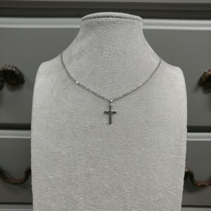 Pode incluir: Um colar de corrente de prata com um pequeno pingente de cruz de prata.