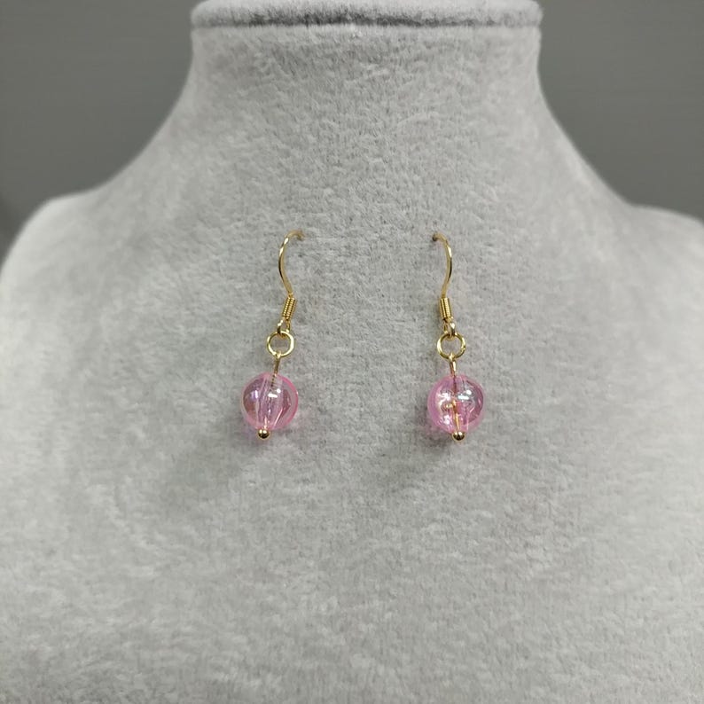 May include: A pair of gold dangle earrings with pink glass beads. The beads have a textured surface and are translucent.