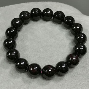 May include: A black gemstone bracelet with round beads. The beads are polished and have a slight shine.