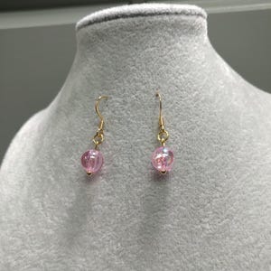 May include: A pair of gold dangle earrings with pink iridescent glass beads.