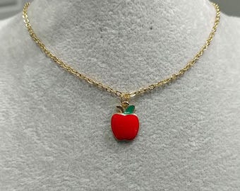 Puede incluir: Un collar de cadena dorada con un colgante de manzana roja. La manzana tiene una hoja y un tallo verdes.