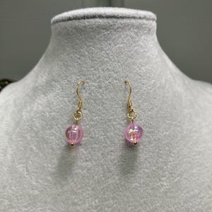 May include: A pair of gold dangle earrings with pink iridescent glass beads.