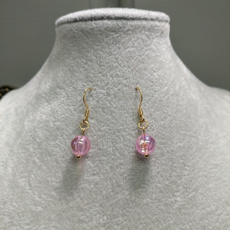 May include: A pair of gold dangle earrings with pink iridescent glass beads.