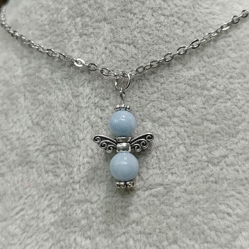 May include: A silver-toned necklace featuring a pendant in the shape of an angel. The angel has light blue bead body and wings. The necklace chain is also silver-toned.
