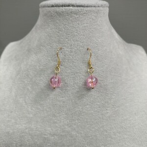 May include: A pair of gold dangle earrings with pink glass beads. The beads are round and have a slight shimmer.