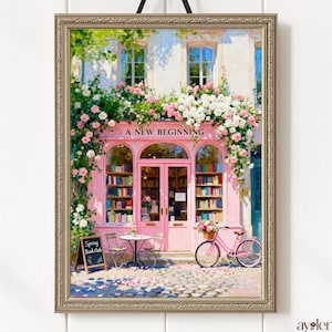 以下が含まれることがあります： 「A New Beginning」の文字が入ったピンク色の本屋の額入りプリント。建物は花で飾られ、外には自転車があります。「Spring Book Club」と書かれた看板があります。