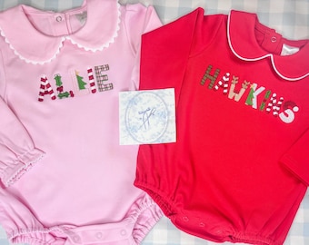 May include: Two baby rompers, one pink and one red, with long sleeves and white scalloped collars. The pink romper has the name "ALLIE" embroidered in colourful letters. The red romper has the name "HAWKINS" embroidered in colourful letters.