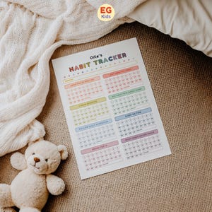 May include: A colorful habit tracker titled "Ollie's Habit Tracker" with sections for daily tasks like reading, exercise, and healthy eating. The tracker is on a beige surface with a teddy bear and a cream-colored blanket in the background. The "EG Kids" logo is in the top right corner.