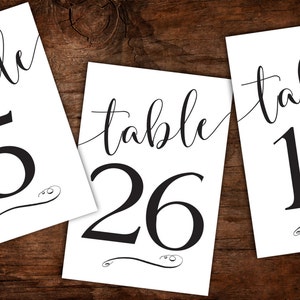 May include: Three white table number cards with black calligraphy. The cards read "table 5", "table 26", and "table 18".