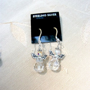 Puede incluir: Un par de pendientes de &aacute;ngel de plata de ley. Cada pendiente presenta un cuerpo de cristal transparente y facetado, alas plateadas y una peque&ntilde;a cabeza de cristal. Los pendientes se exhiben en una tarjeta negra con "STERLING SILVER".