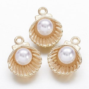 May include: Three gold-tone metal charms shaped like seashells with a white pearl in each. The charms have a loop at the top for attaching to a necklace or bracelet.
