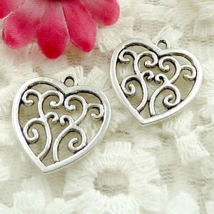 以下が含まれることがあります： 繊細で複雑なデザインの銀製のフィリグリーハートチャーム2個。チャームは、ジュエリープロジェクトにエレガントなタッチを加えるのに最適です。