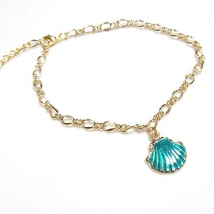 May include: A gold-toned metal chain anklet featuring a single dangling seashell charm. The charm is finished with a vibrant turquoise enamel coating that highlights the textured ridges of the shell. The chain includes a lobster clasp and extender.