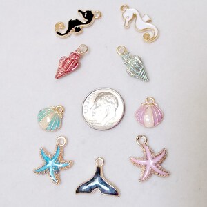 May include: Assortment of 10 gold-tone metal charms with enamel detailing. The charms feature seahorse, seashell, starfish, and whale tail designs in various colours, including pink, blue, green, white, and black.