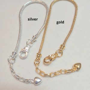 May include: Two snake chain bracelets, one silver and one gold, with heart charms and lobster claw clasps. The bracelets are labeled "silver" and "gold".
