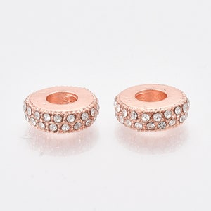 May include: Two rose gold spacer beads with clear crystal accents. The beads are round and have a hole in the center.