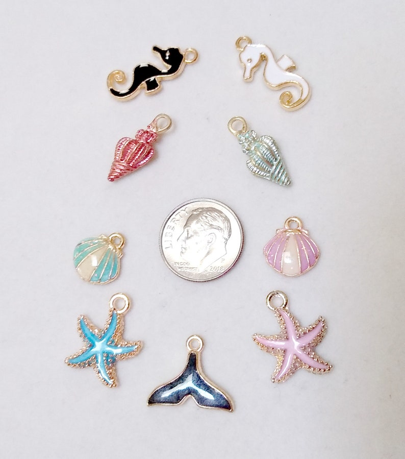 May include: Assortment of 10 gold-tone metal charms with enamel detailing. Charms include a seahorse, starfish, seashell, and a whale tail. The charms are perfect for jewellery making, scrapbooking, and other craft projects.