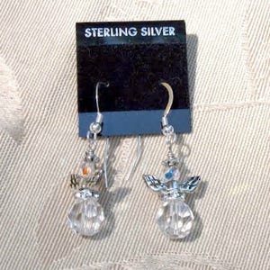 Puede incluir: Un par de pendientes de &aacute;ngel de plata de ley. Cada pendiente presenta un cuerpo de cristal transparente facetado, alas plateadas y una peque&ntilde;a cuenta colorida en la parte superior. Los pendientes cuelgan de ganchos plateados y se exhiben en una tarjeta negra que dice "STERLING SILVER".
