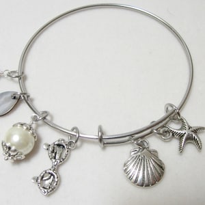 May include: Silver bangle bracelet with multiple charms, including a pearl, seashell, starfish, and a pair of glasses.