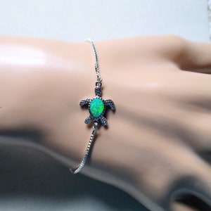 May include: A silver chain bracelet with a green opal turtle charm.