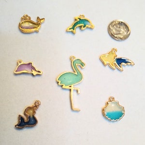 May include: Assortment of seven gold-tone metal charms with colorful resin inlays. The charms feature a whale, two dolphins, a flamingo, a fish, a mermaid, and a seashell.