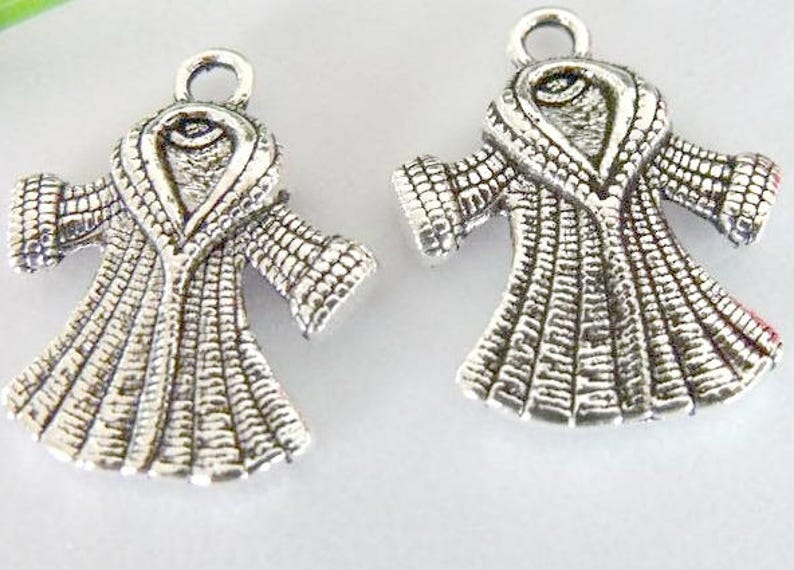 May include: Two silver-toned metal charms shaped like a robe with a large collar. The charms have a textured surface and are perfect for adding a unique touch to jewelry projects.