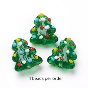 May include: Four green glass Christmas tree beads with white, red, blue, and yellow accents.  The beads are approximately 1 inch tall.