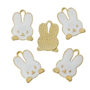 May include: Five gold-coloured metal charms shaped like bunnies. Four of the charms are white with gold accents and have a bunny face with closed eyes. One charm is gold with a textured surface and has a bunny silhouette.