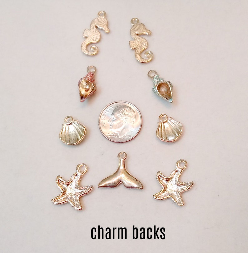 May include: A collection of gold and silver charm backs featuring seahorse, seashell, starfish, and mermaid tail designs. The charms are arranged on a white surface with a 10 pence coin for scale.