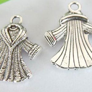 May include: Two silver charm pendants in the shape of robes. One robe has a large collar and the other has a more fitted style.