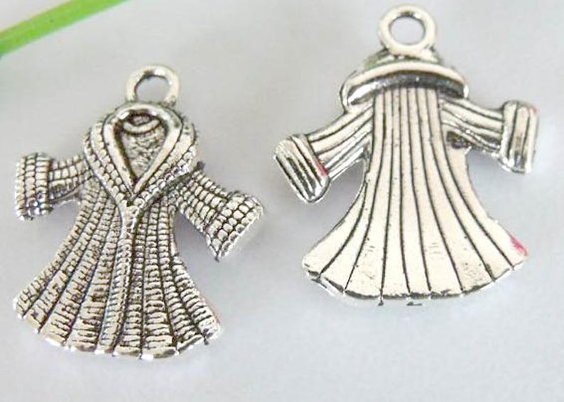 May include: Two silver charm pendants in the shape of robes. One robe has a large collar and the other has a more fitted style.