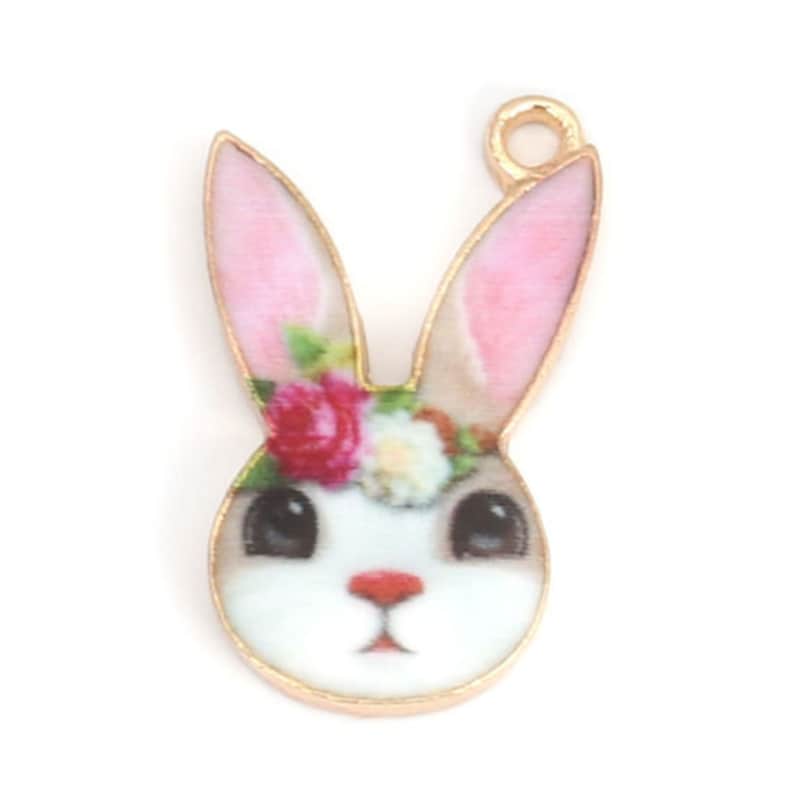 K&ouml;nnte beinhalten: Goldfarbener Metall-Anh&auml;nger mit einem wei&szlig;en Kaninchen mit rosa Ohren und einer Blumenkrone. Das Kaninchen hat braune Augen und eine rosa Nase.