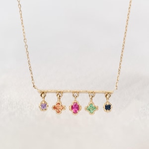 May include: A gold chain necklace with a bar pendant and five dangling charms, each featuring a different coloured gemstone: purple, orange, pink, green, and blue.