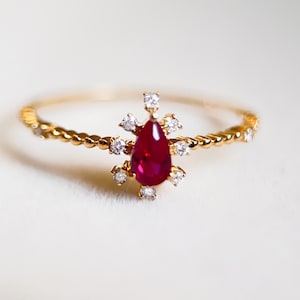 May include: A gold ring with a twisted band and a pear-shaped ruby gemstone surrounded by smaller diamonds.